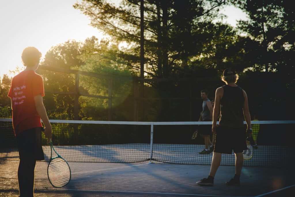 Three young men playing tennis on an outdoor court at sunset, capturing a vibrant and active moment.